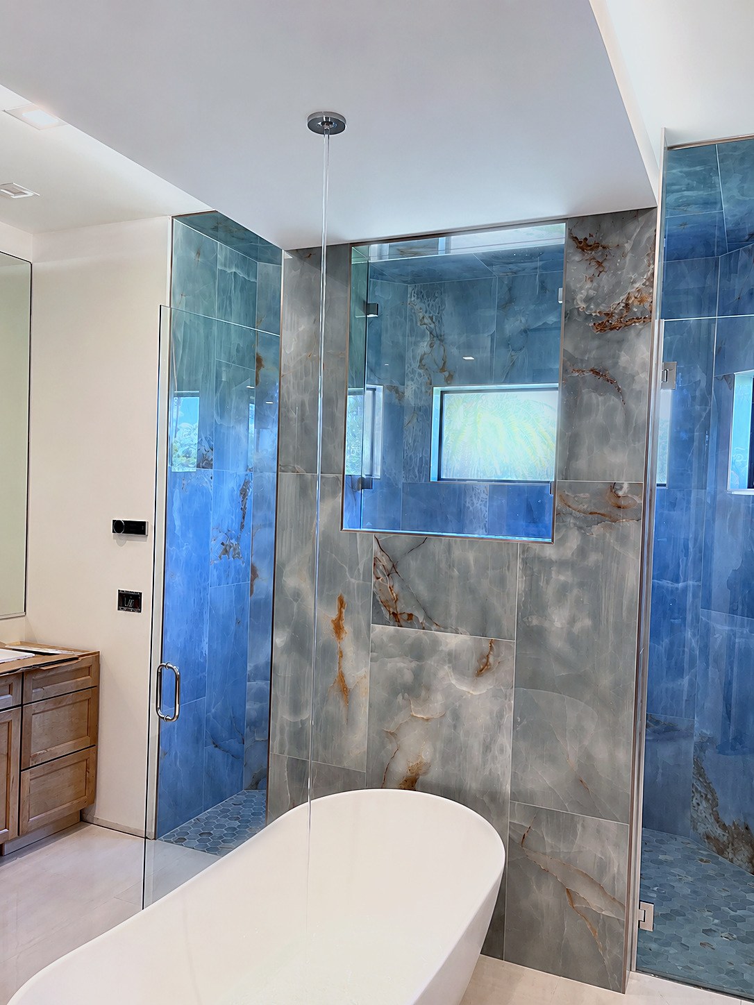 Finished primary bathroom with marble-look shower tile and freestanding soaking tub