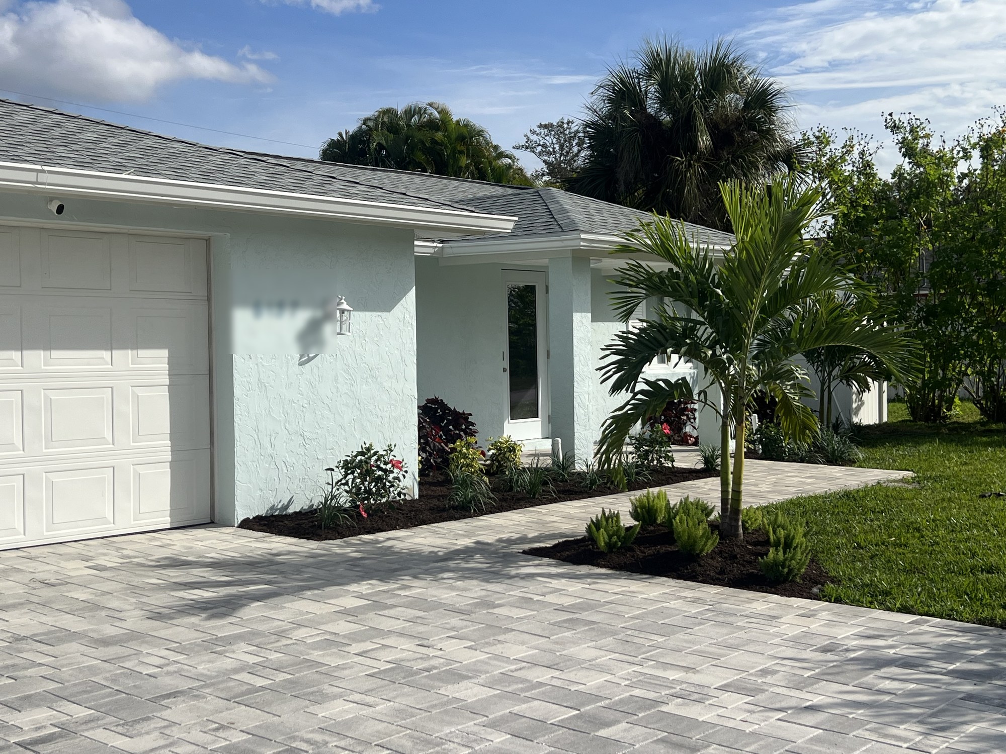 Finished exterior of a whole-home remodel with new paint, paver driveway, and landscaping in Florida